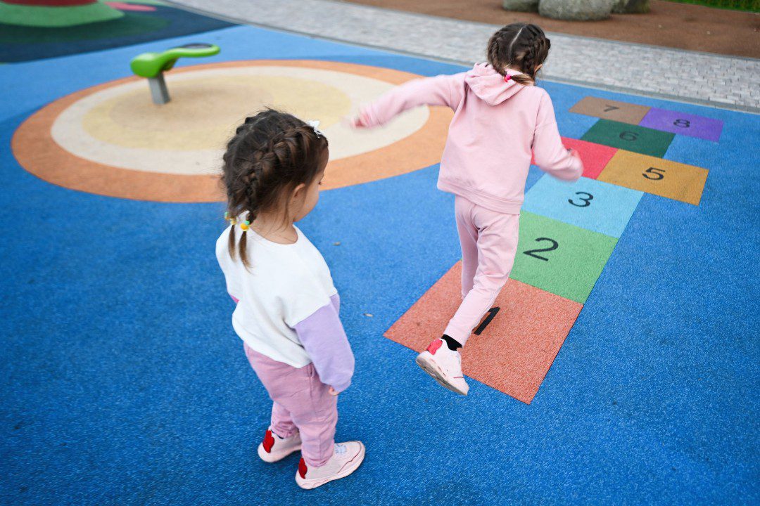 Preschool children take turns playing hopscotch.